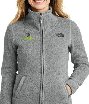Woman wearing a gray North Face jacket with a zipper and pockets. The jacket has embroidered logos: one for Paul Harris Fellows in green on the left and The North Face on the right.