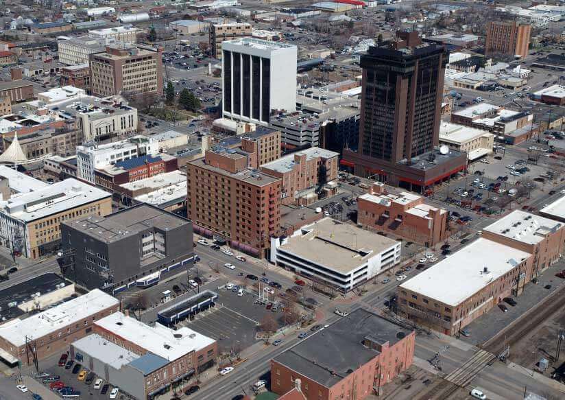 Aerial view of a city's downtown area featuring a mix of mid-rise and low-rise buildings, parking lots, and streets with light traffic. Billings, Montana