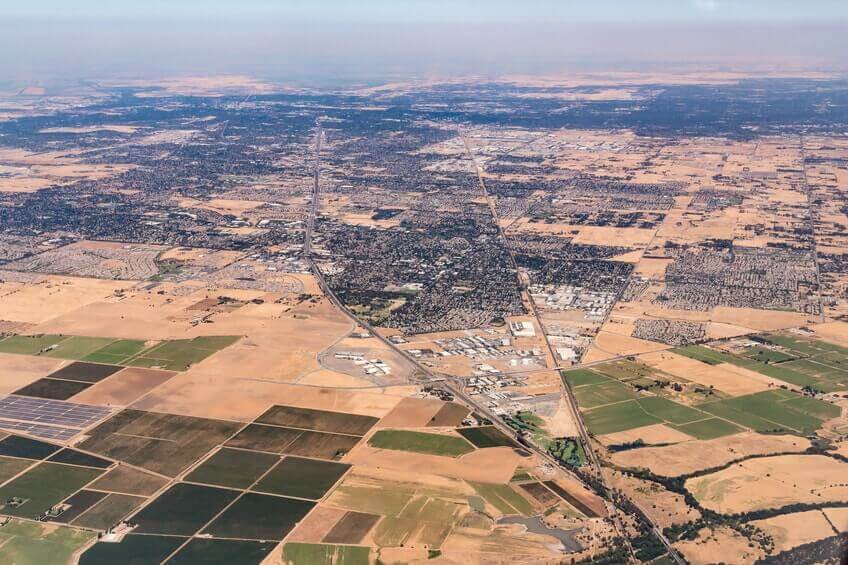 Aerial view of a cityscape with a mix of urban areas, roads, and agricultural fields, showing grid-like patterns of streets and land parcels. Aerial view of a cityscape with a mix of urban areas, roads, and agricultural fields, showing grid-like patterns of streets and land parcels.