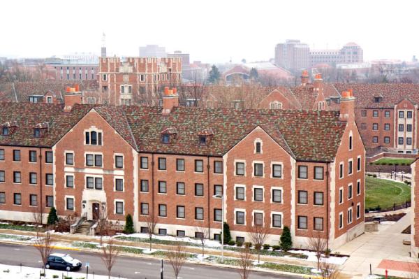 View of a large brick building with multiple windows, snow on the ground, and several other buildings visible in the background on a foggy day. View of a large brick building with multiple windows, snow on the ground, and several other buildings visible in the background on a foggy day.