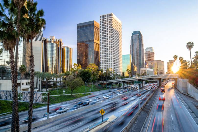Sunset view of a busy freeway with blurred traffic in front of downtown skyscrapers and palm trees in Los Angeles. Sunset view of a busy freeway with blurred traffic in front of downtown skyscrapers and palm trees in Los Angeles.
