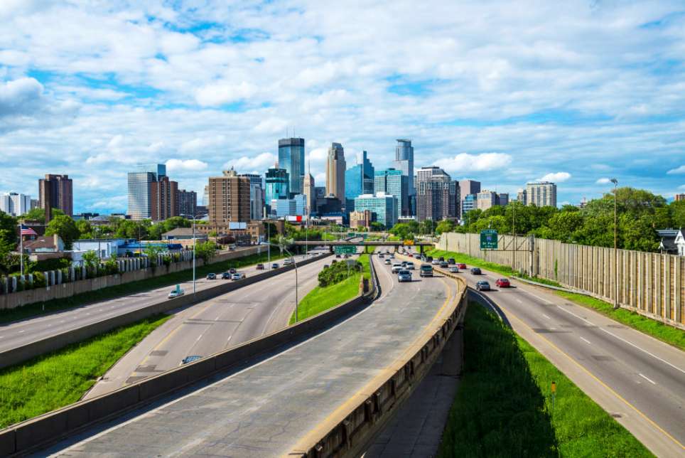 View of a highway leading to a city skyline with modern skyscrapers and a partly cloudy sky. View of a highway leading to a city skyline with modern skyscrapers and a partly cloudy sky.